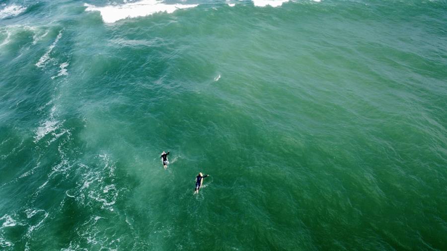 Surfeurs au large dans une eau turquoise, vue aérienne par drone